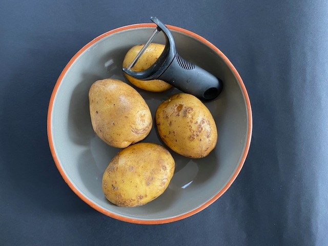 Unpeeled potatoes with a potato peeler